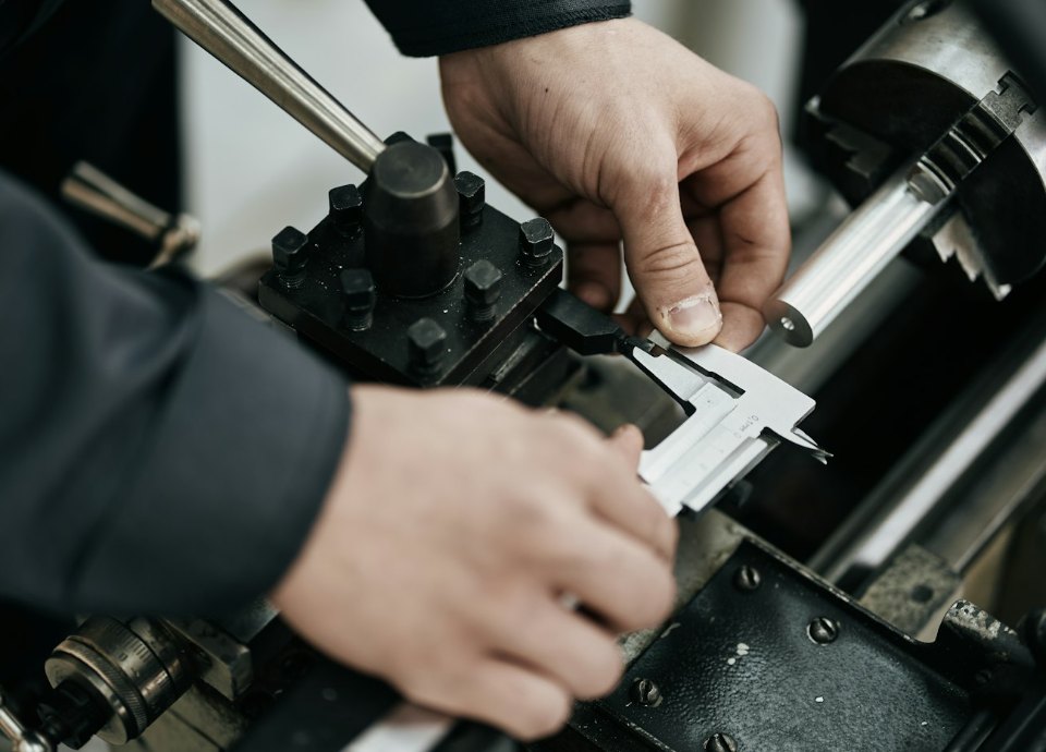 Operator measuring a turned part with a caliper at the lathe